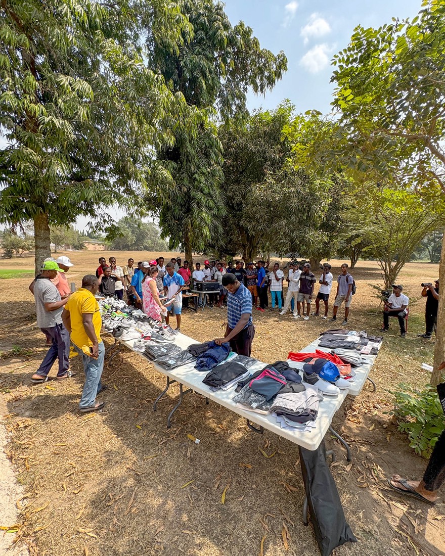 Lange Tische mit Golfschuhen, Polos und Hosen, dahinter warten die Caddies